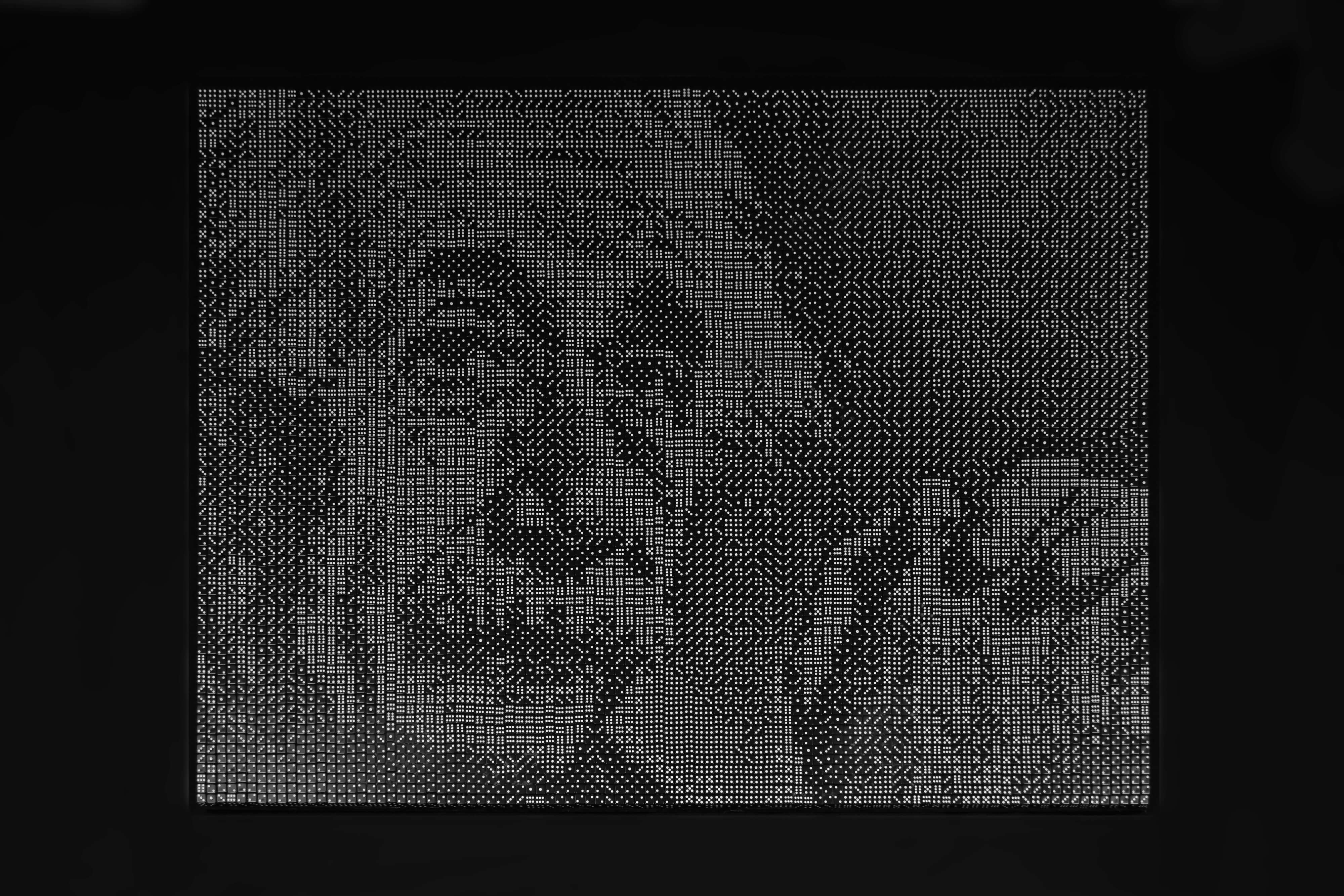 Een mozaïek van zwarte dobbelstenen met witte ogen op een zwarte achtergrond. Het mozaïek laat het gelaat en de gevouwen handen van Albert Einstein zien, die met een vriendelijke rustige blik de camera inkijkt.