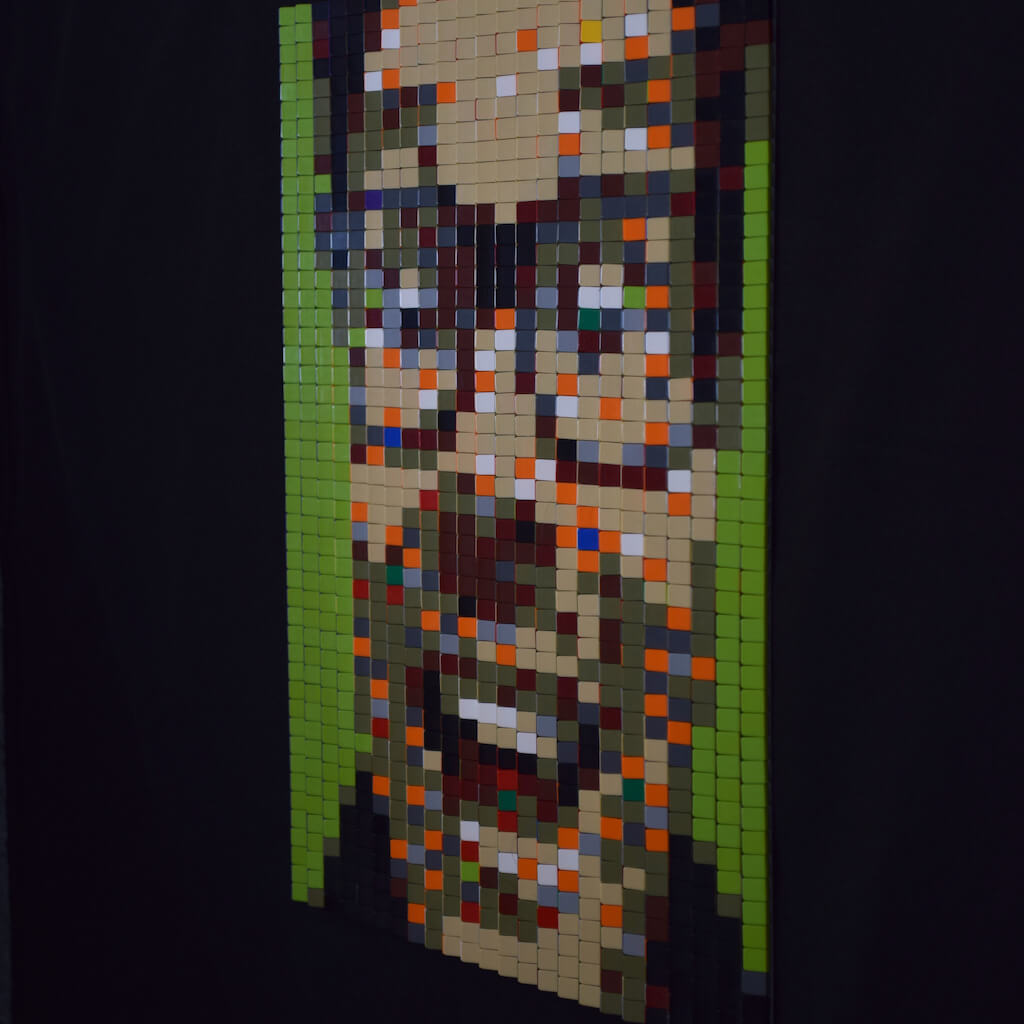 thumbnail - Zijaanzicht (links) van een tabula scalata van legosteentjes. Het kleurrijke portret van een lachende, brildragende man van middelbare leeftijd op een felgroene achtergrond.